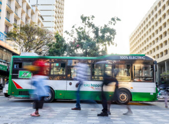 An Electric bus parked in the Streets of Nairobi. People Crossing on the foreground.
