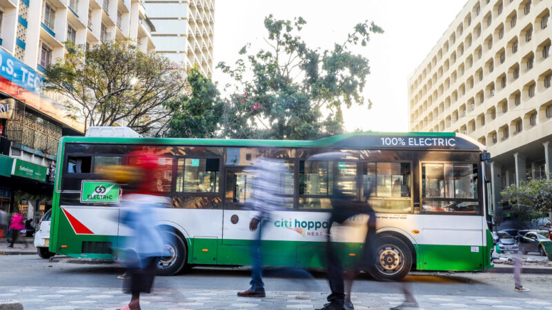 An Electric bus parked in the Streets of Nairobi. People Crossing on the foreground.