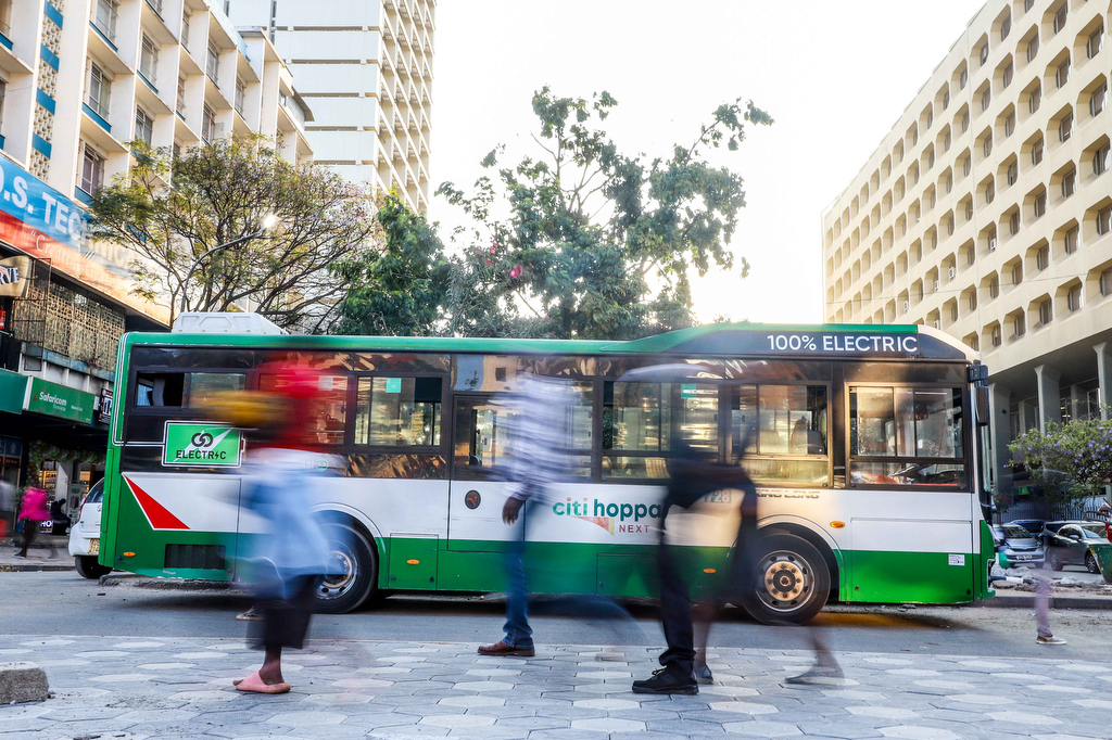 An Electric bus parked in the Streets of Nairobi. People Crossing on the foreground.